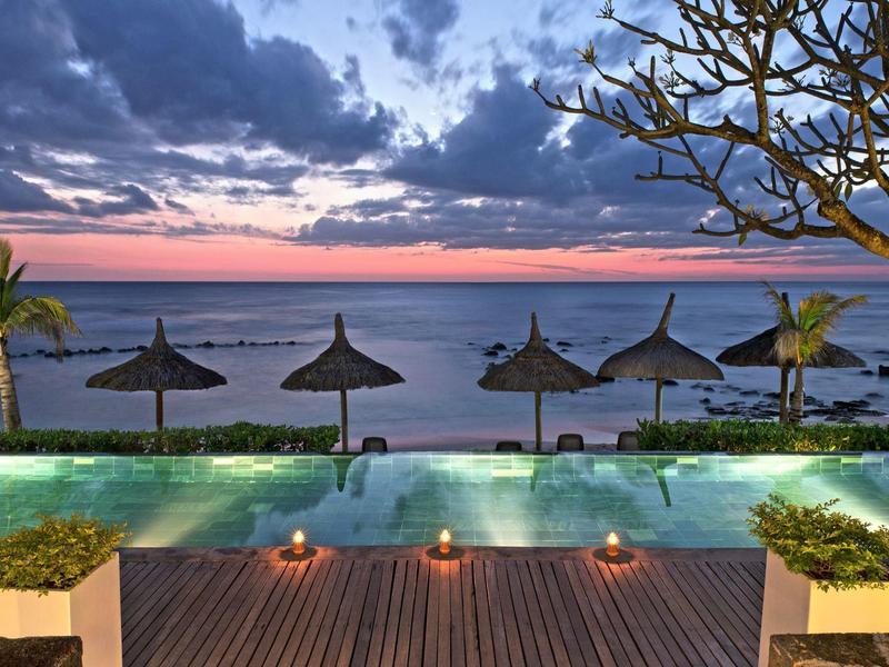 Area piscina con vista sul mare al tramonto, con palme e ombrelloni di paglia.