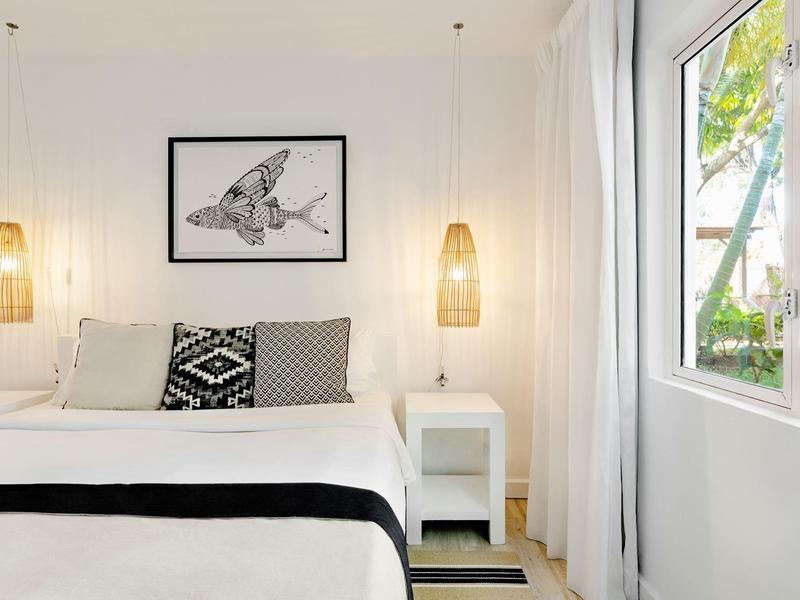 Camera luminosa con letto matrimoniale, due comodini, quadro di pesce e finestra con vista sul verde.