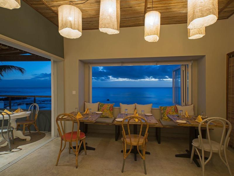 Accogliente sala da pranzo con vista mare al crepuscolo, illuminata da lampade a sospensione.