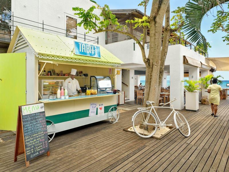 Area ricreativa con chiosco di cibo e opera d'arte di bicicletta bianca su terrazza in legno al sole.