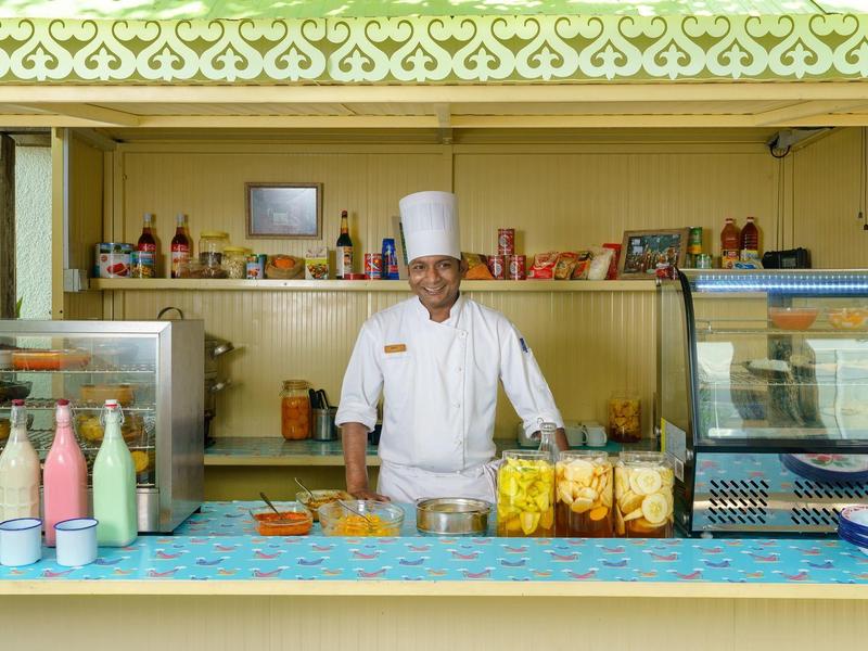 Uno chef in abiti bianchi è dietro una bancarella con vari cibi e bevande.