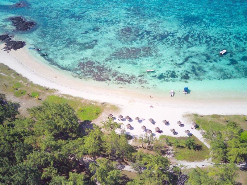 Aerial view of a beach with clear blue water, sand, and sun umbrellas next to a forest.
