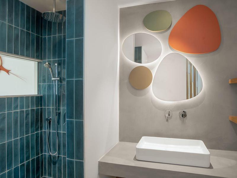 Modern bathroom with blue tiled shower area and creative mirror above sink.
