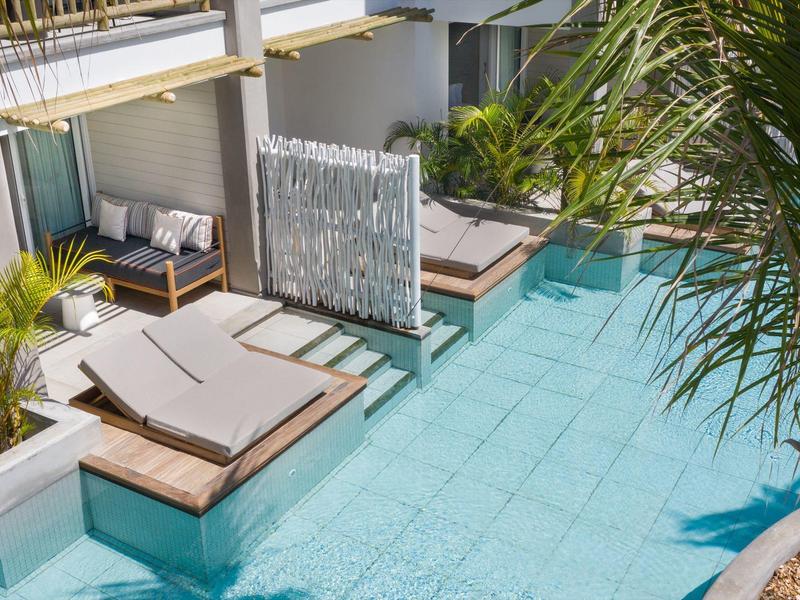 Luxurious outdoor lounge with pool, sunbeds, and plants in a tropical setting.