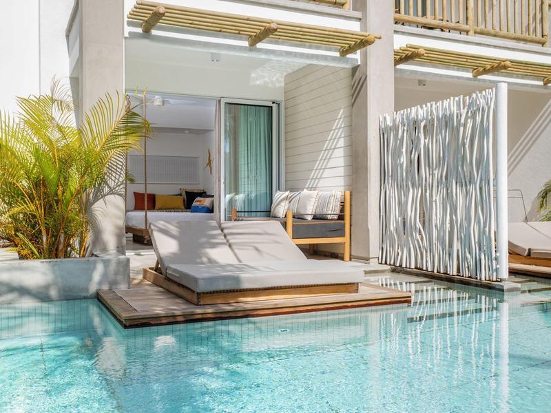 Modern outdoor area with pool, sun loungers, and garden by a hotel room.