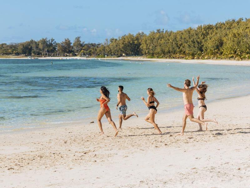 Five people running along the beach with a forested coastline in the background.