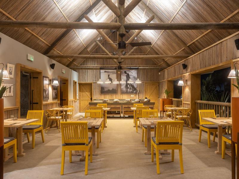 Bright restaurant with wooden ceiling, wooden furniture, and symmetrically arranged tables and chairs.