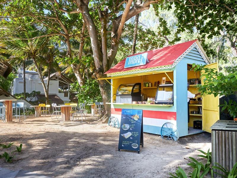 Colorful snack stand under trees with outdoor tables and chairs.