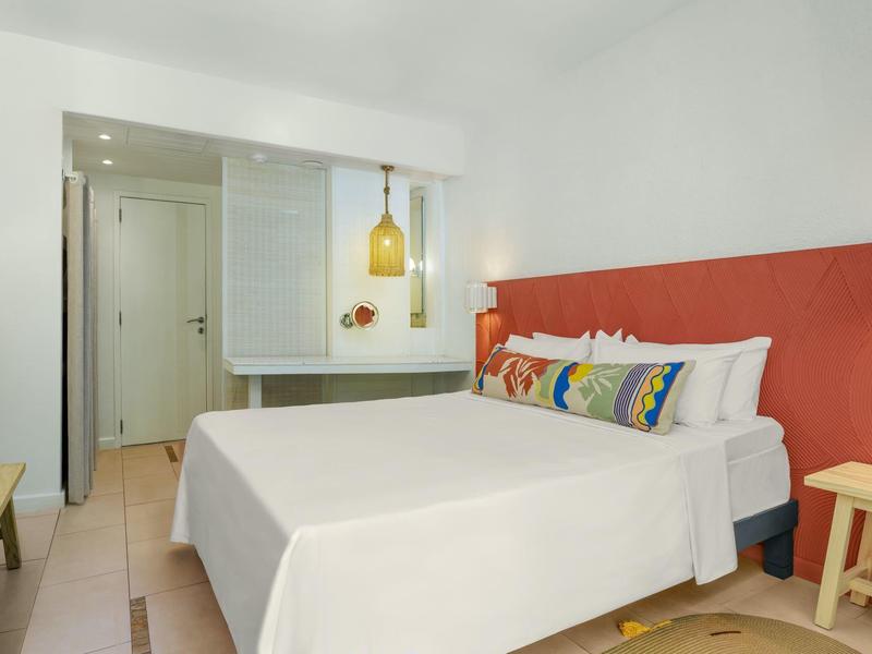 Simple hotel room with double bed, colorful pillows, and modern bathroom.