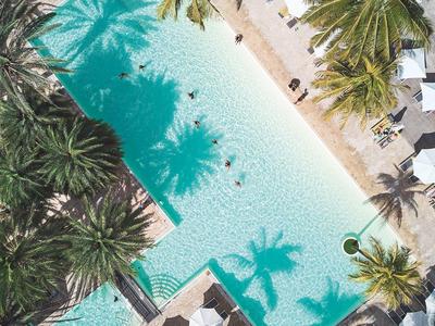 Letecký pohled na obdélníkový bazén s palmami a slunečníky v tropickém letovisku.