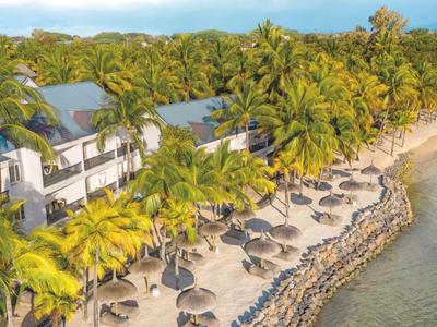 Plážový hotel s palmami, lehátky a slunečníky u klidné vody