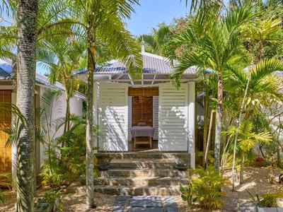 Tropický prázdninový dům s bílými posuvnými dveřmi, obklopený palmami a bujnou zelení.