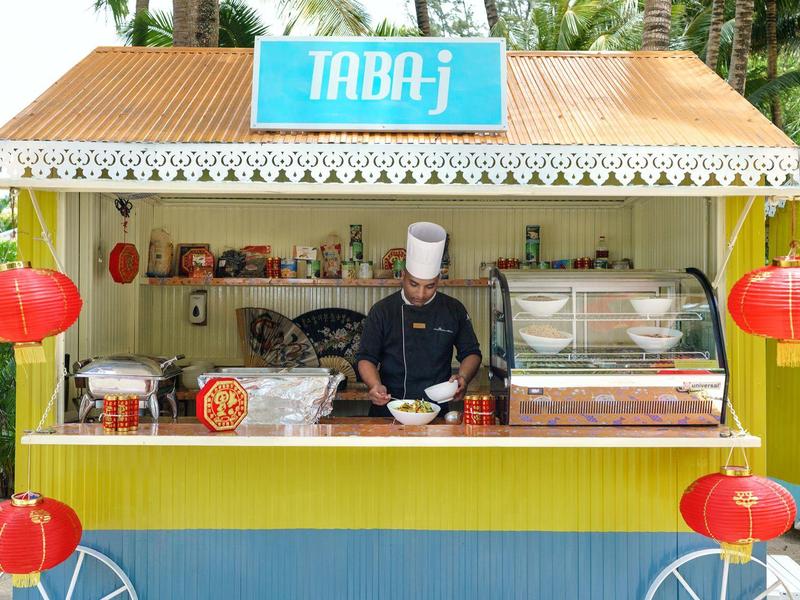 Kuchař připravuje jídlo v barevném malém pouličním stánku s červenými ozdobami.