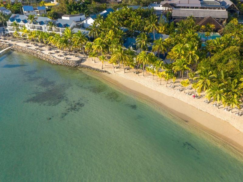 Letecký pohled na tropickou pláž s čistou vodou, bílým pískem a bujnou vegetací.