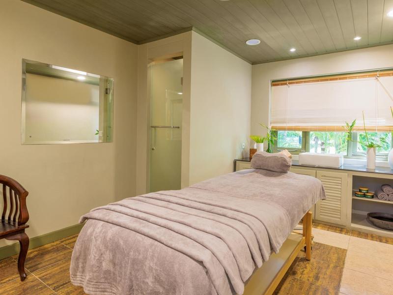 Relax zóna s masážním stolem, židlí a oknem s rostlinami v wellness místnosti.