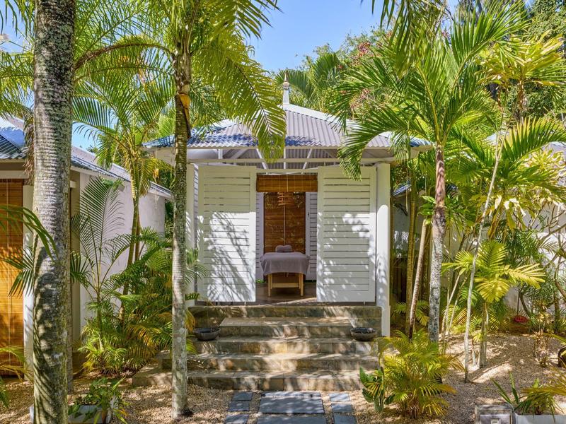 Tropický prázdninový dům s bílými posuvnými dveřmi, obklopený palmami a bujnou zelení.