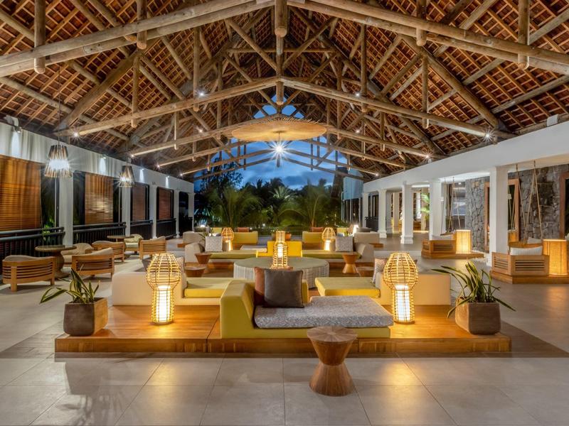 Otevřená lounge zóna s pohodlnými pohovkami a lampami pod dřevěnou střechou v hotelu.