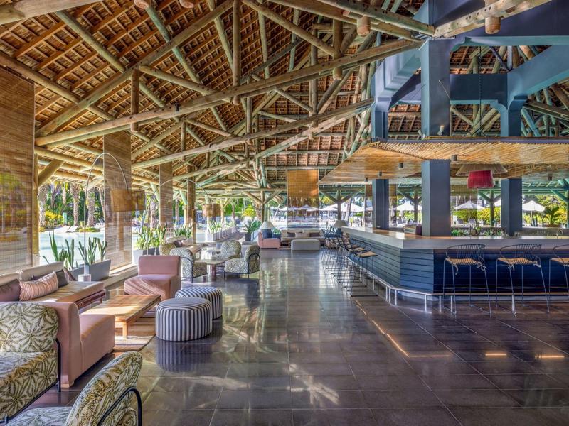 Otevřená hotelová lounge s moderním posezením a barem pod dřevěnou střechou.