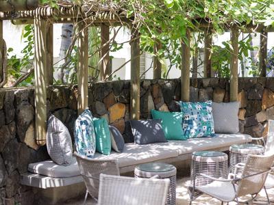 Gemütliche Außensitzecke mit gepolsterten Sitzgelegenheiten und Pflanzen überdacht.