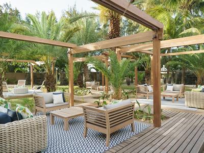 Przytulna przestrzeń na świeżym powietrzu z drewnianą konstrukcją, sofami i palmami w tle.