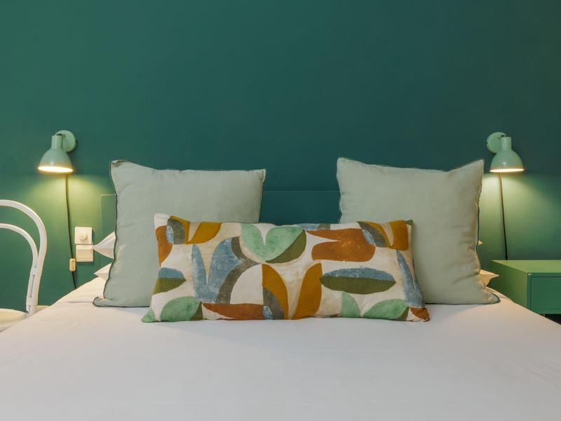 Modernes Hotelzimmer mit grünem Kopfteil, zwei Lampen und buntem Kissen auf weißem Bett