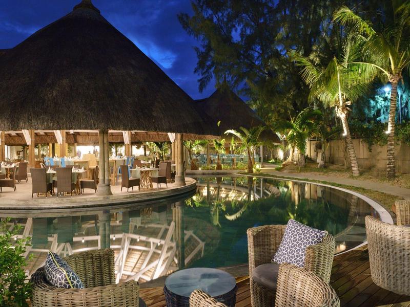 Abendliche Lounge mit runden Sitzgruppen und beleuchtetem Pool in tropischem Hotelresort.