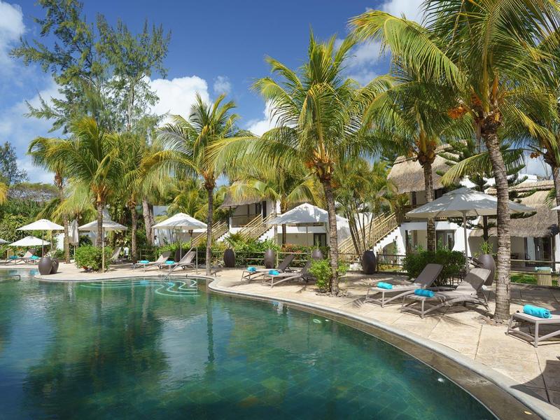 Tropischer Poolbereich mit Liegestühlen und Palmen unter blauem Himmel.