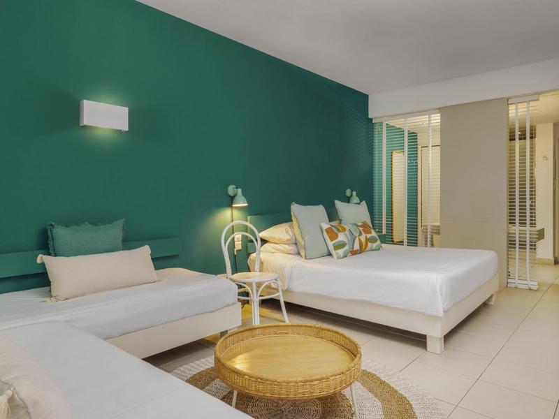 Moderner Hotelzimmer mit grünem Akzentwand, Doppelbett, Sofa und kleiner runder Tisch.