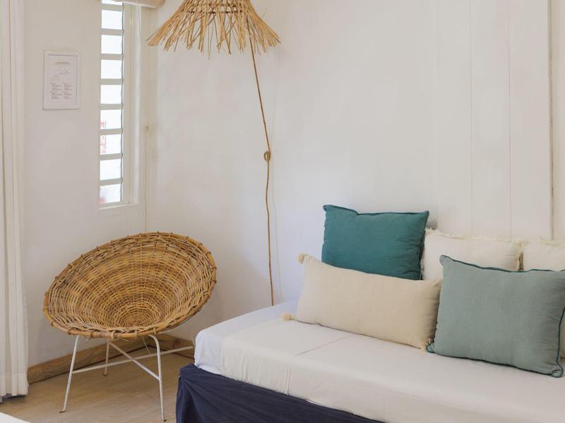 Gemütliche Sitzecke mit einem weißen Sofa, Kissen und einem runden Korbstuhl vor weißer Wand.