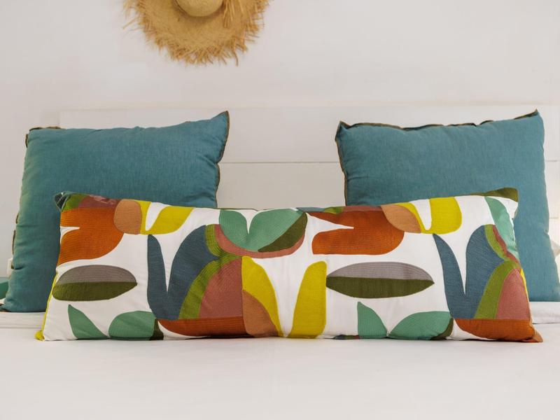 Drei dekorative Kissen auf einem weißen Bett mit einem Strohhut an der Wand.