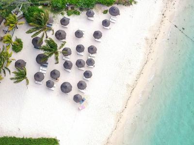 Letecký pohled na tropickou pláž s deštníky a průzračnou tyrkysovou vodou.