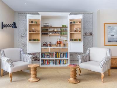 Gemütlicher Sitzbereich mit zwei weißen Sesseln, kleinem Holztisch und offenem Regal voller Bücher in einem hellen Raum.