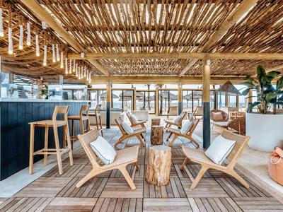 Accogliente lounge esterna con sedie e tavoli in legno e tetto naturale in listelli di legno.