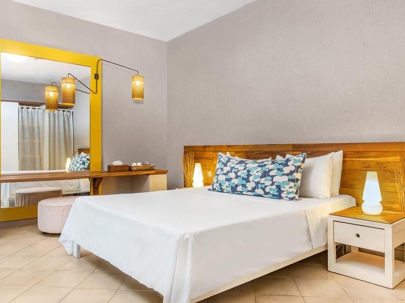 Světle zařízená ložnice s velkou postelí, dřevěným nábytkem a moderním osvětlením.