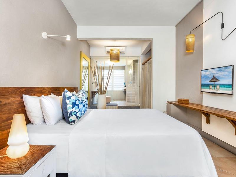 Světý hotelový pokoj s velkou postelí, dřevěnými doplňky a televizí na zdi.