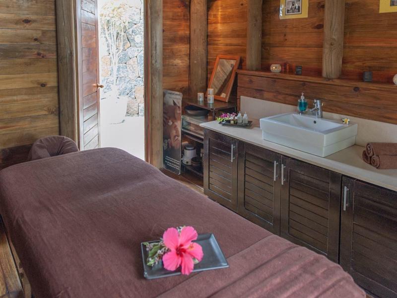 Příjemná masážní místnost s dřevěnými stěnami, hnědým masážním stolem a umyvadlem v relaxační zóně.