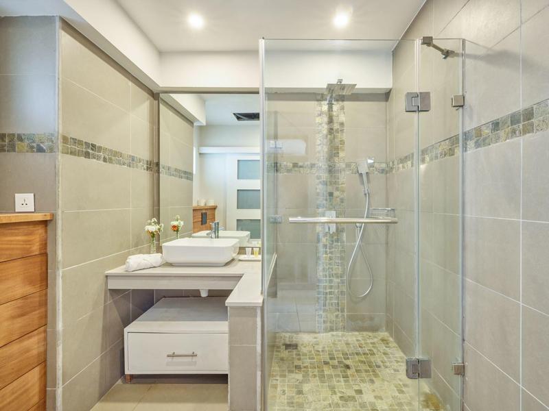 Moderní koupelna s bezbariérovým sprchovým koutem, umyvadlem a světlými dlaždicemi.