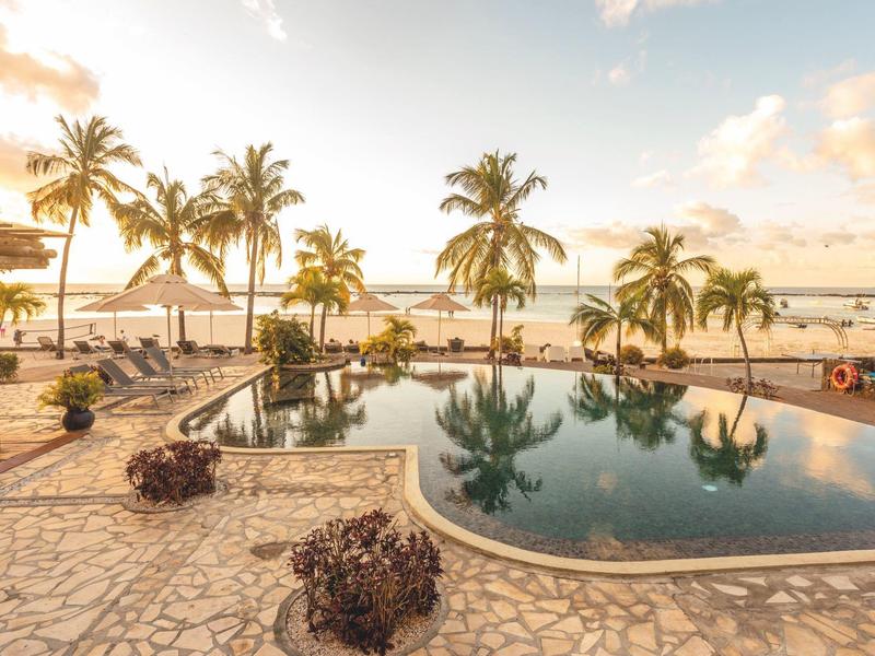 Bazénová zóna s palmami a posezením v tropickém resortu při západu slunce.