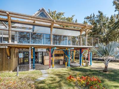 Modernes zweistöckiges Haus mit Holzveranda, Glasgeländer und bunter Spielplatz-Ausrüstung im Garten.