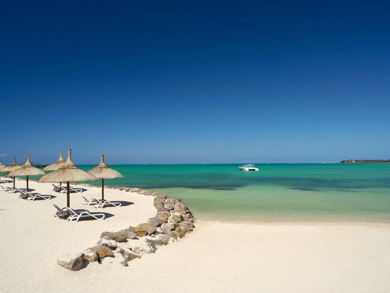 Una tranquila playa de arena con sombrillas de paja y agua turquesa clara bajo un cielo azul.