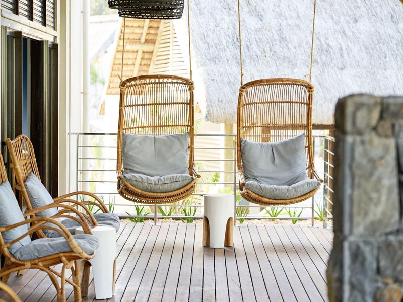 Porche con dos sillones colgantes de mimbre y tres sillas acolchonadas sobre terraza de madera.