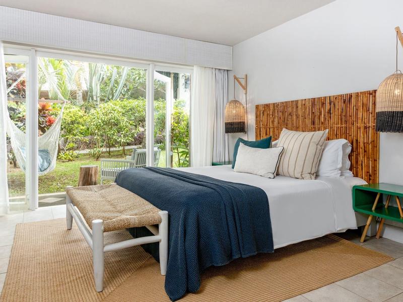 Dormitorio luminoso con cama grande, elementos de madera y vista hacia un jardín.