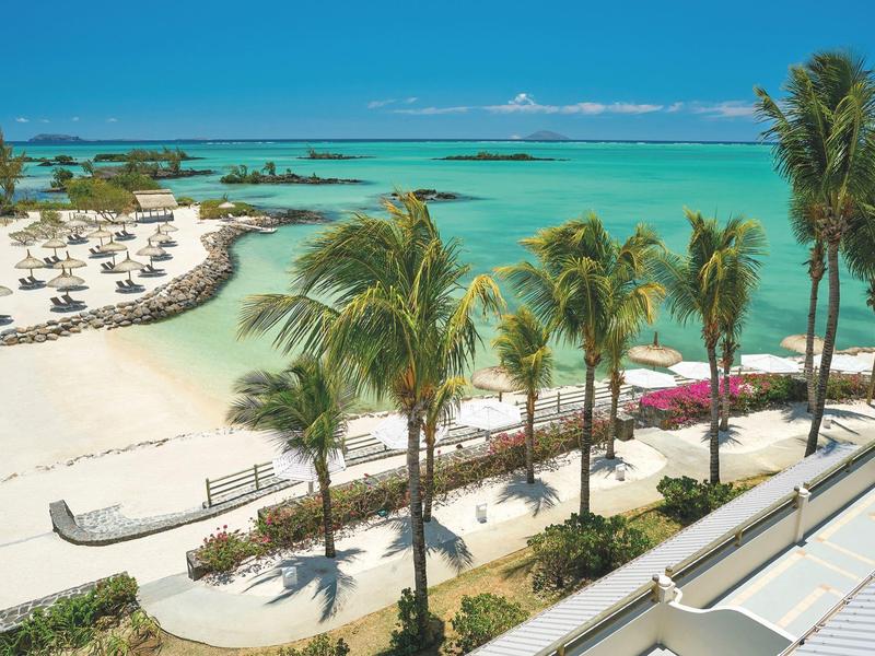 Playa tropical con palmeras, arena blanca, sombrillas y agua turquesa clara junto a un hotel.
