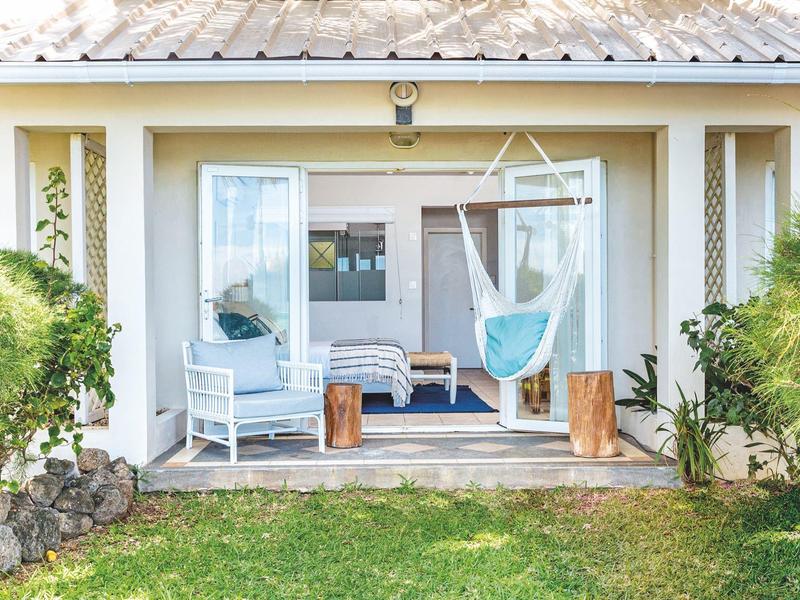 Acogedora veranda con sillón colgante, sillas y mesas de madera frente a una casa de vacaciones.