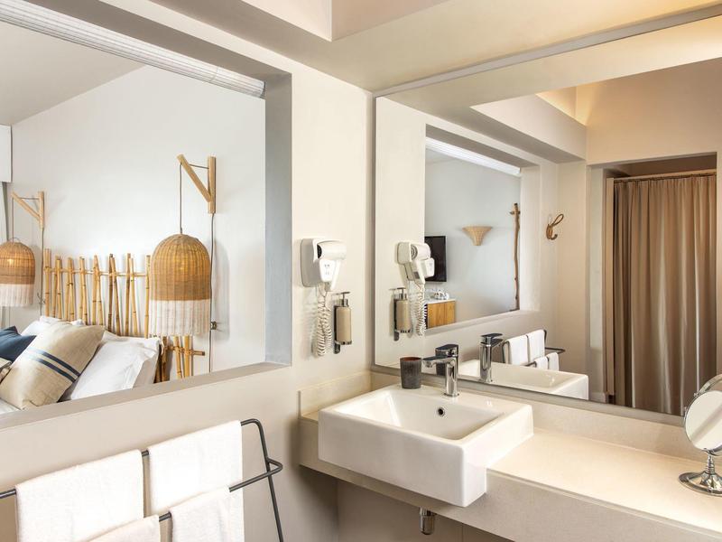 Baño de hotel moderno con gran espejo, lavabo y lámparas de madera elegantes.