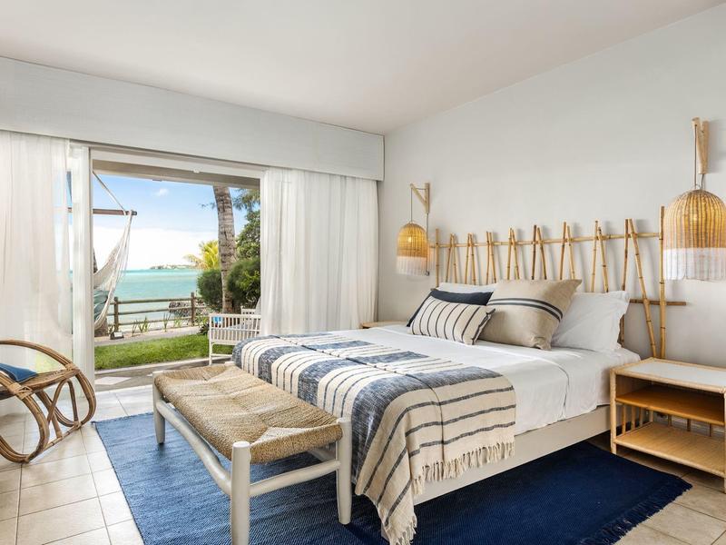 Habitación de hotel luminosa con cama doble, muebles de madera y vista al mar desde el balcón.