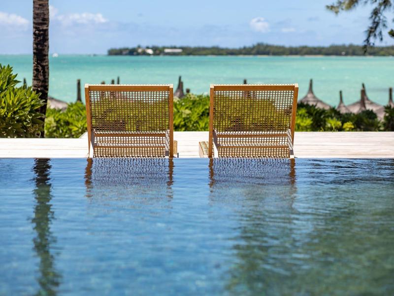 Dos tumbonas junto a una piscina con vistas al mar y vegetación tropical en un día soleado