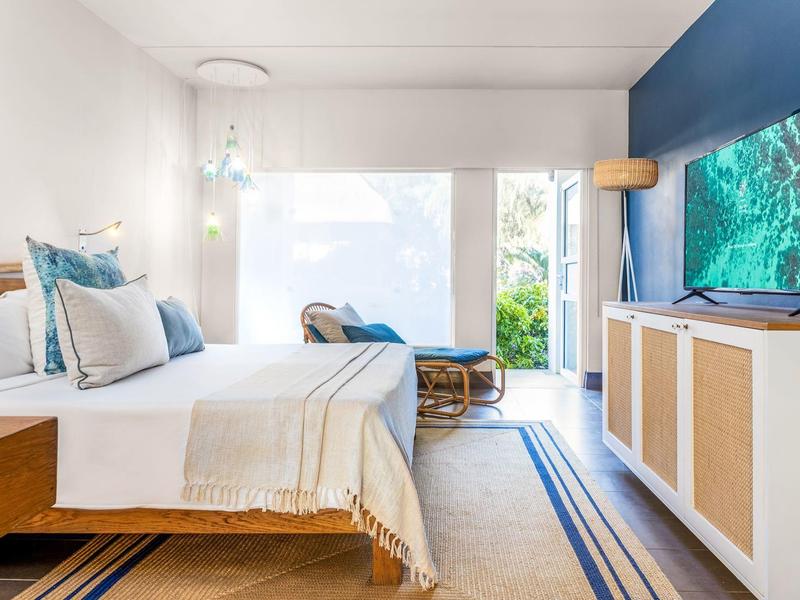 Habitación de hotel luminosa con cama doble, diseño azul y blanco y televisor en la pared.