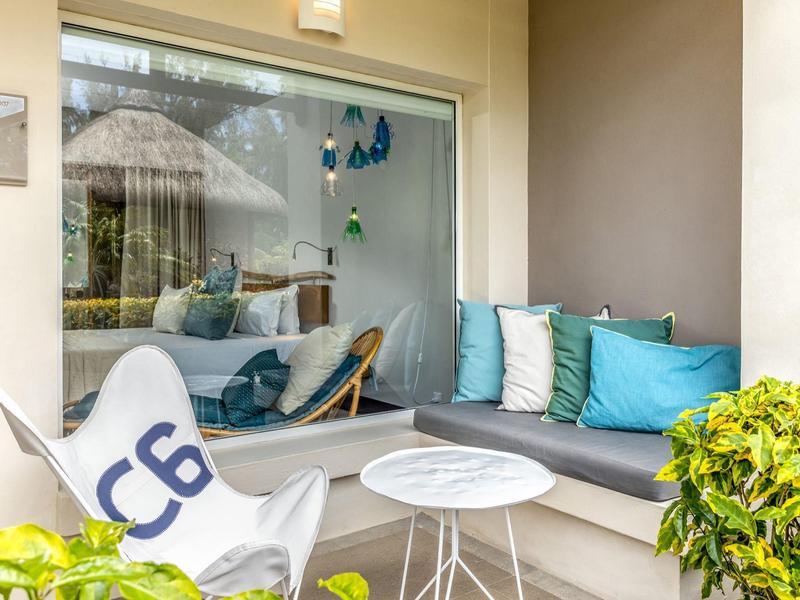 Acogedor rincón lounge con cojines, mesa pequeña y vista a una habitación con silla colgante y decoración.