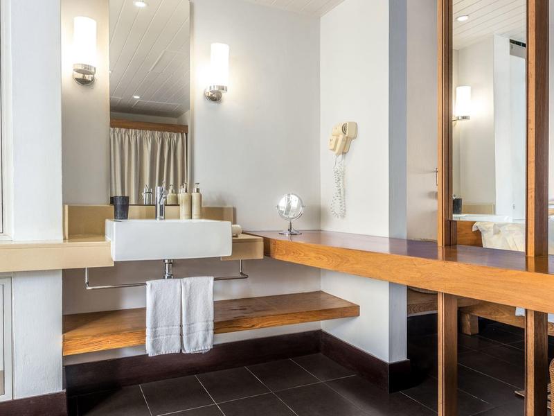 Lavabo moderno de hotel con espejo grande, lavabo integrado y área para sentarse.